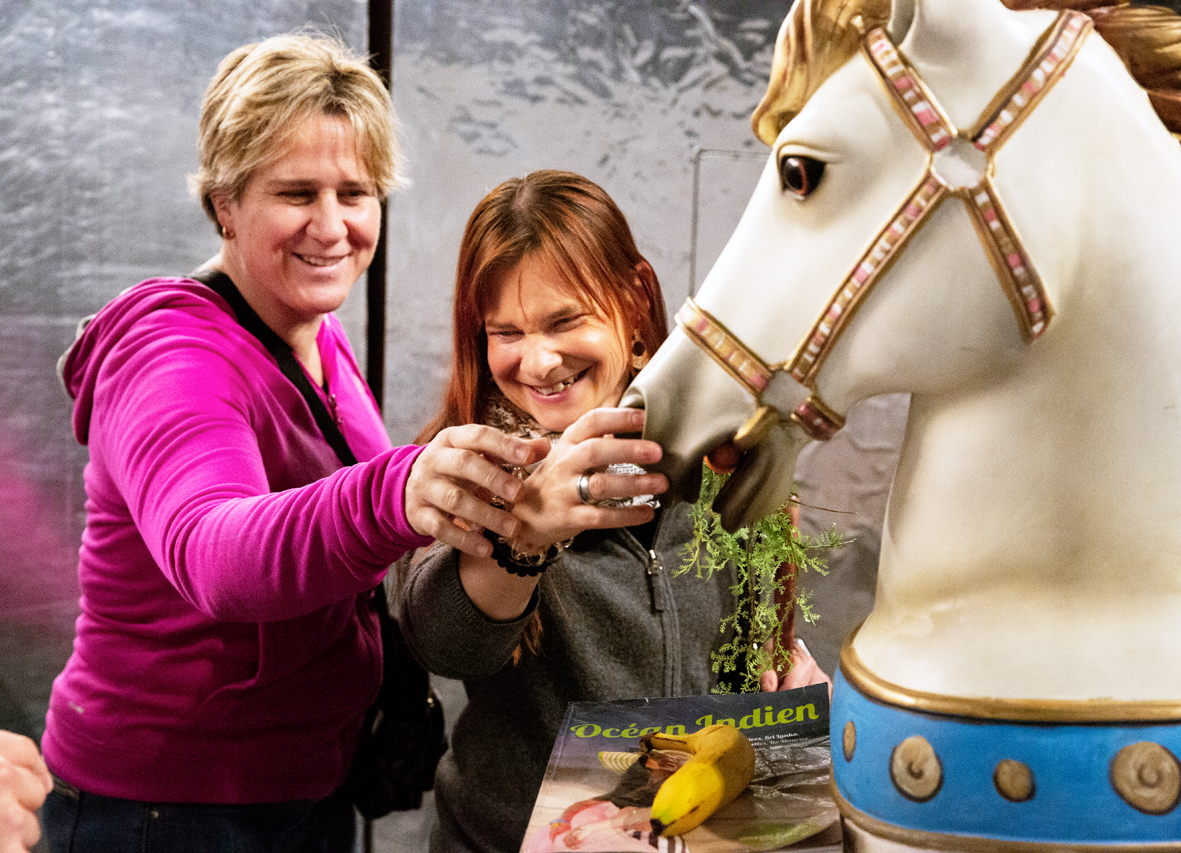 Deux femmes touchent les naseaux d'un cheval de carrousel