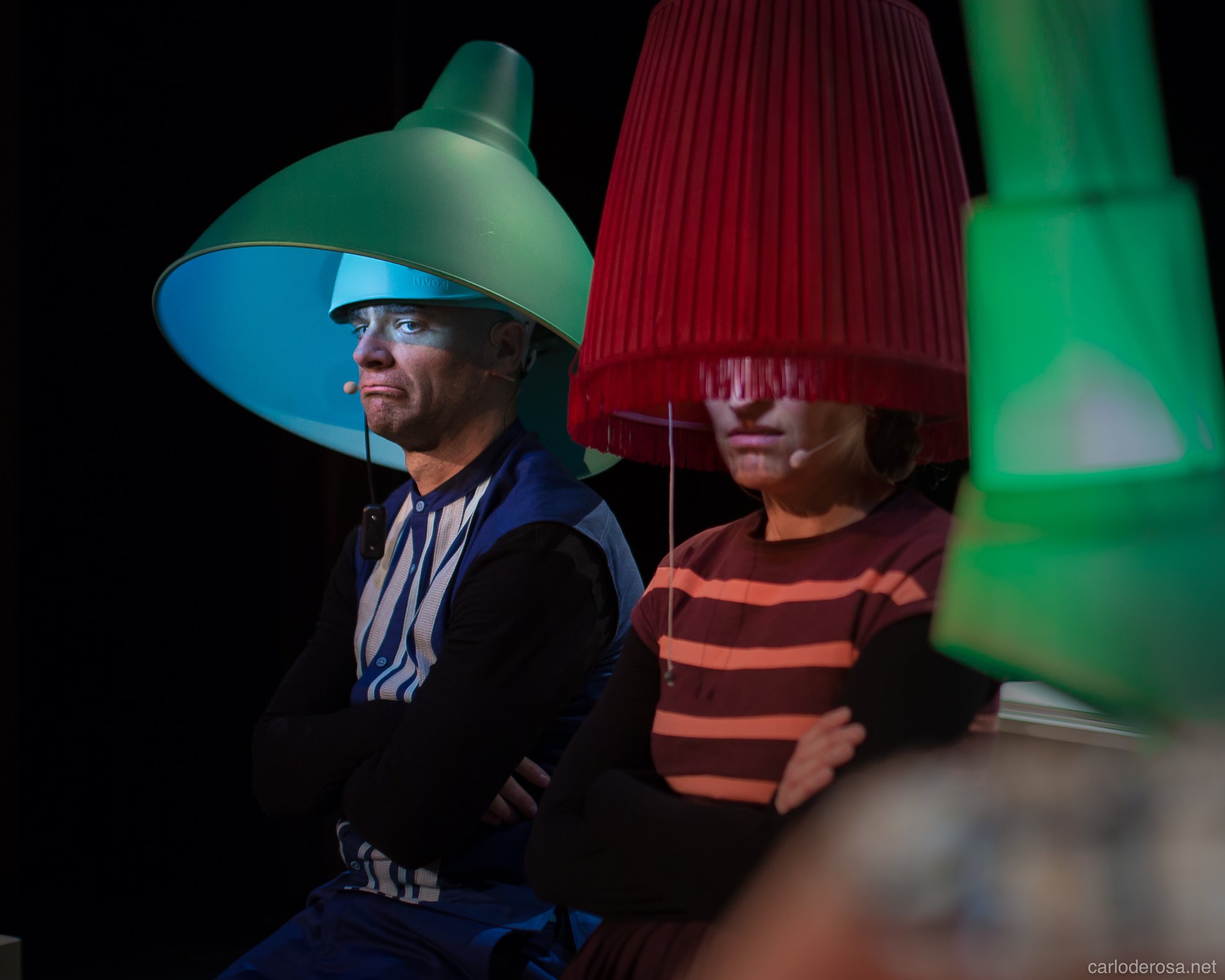 Deux comédiens avec des abat-jours de couleur sur la tête sons côte à côte et semblent fâchés. Il s'agit du papa-lampe et de la maman lampe, parents d'une famille recomposée de 4 petites-lampes.