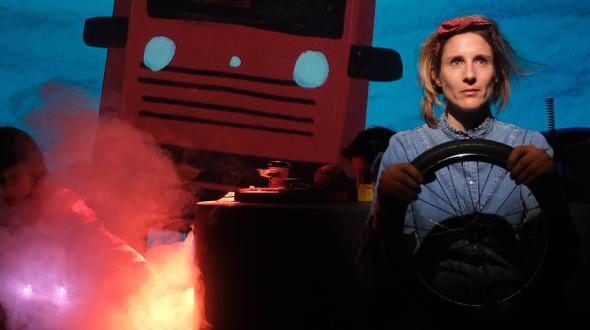 Au premier plan une conductrice vêtue d'une chemise bleue tient son volant, a l'arrière plan un gros camion rouge semble lui foncer dessus.