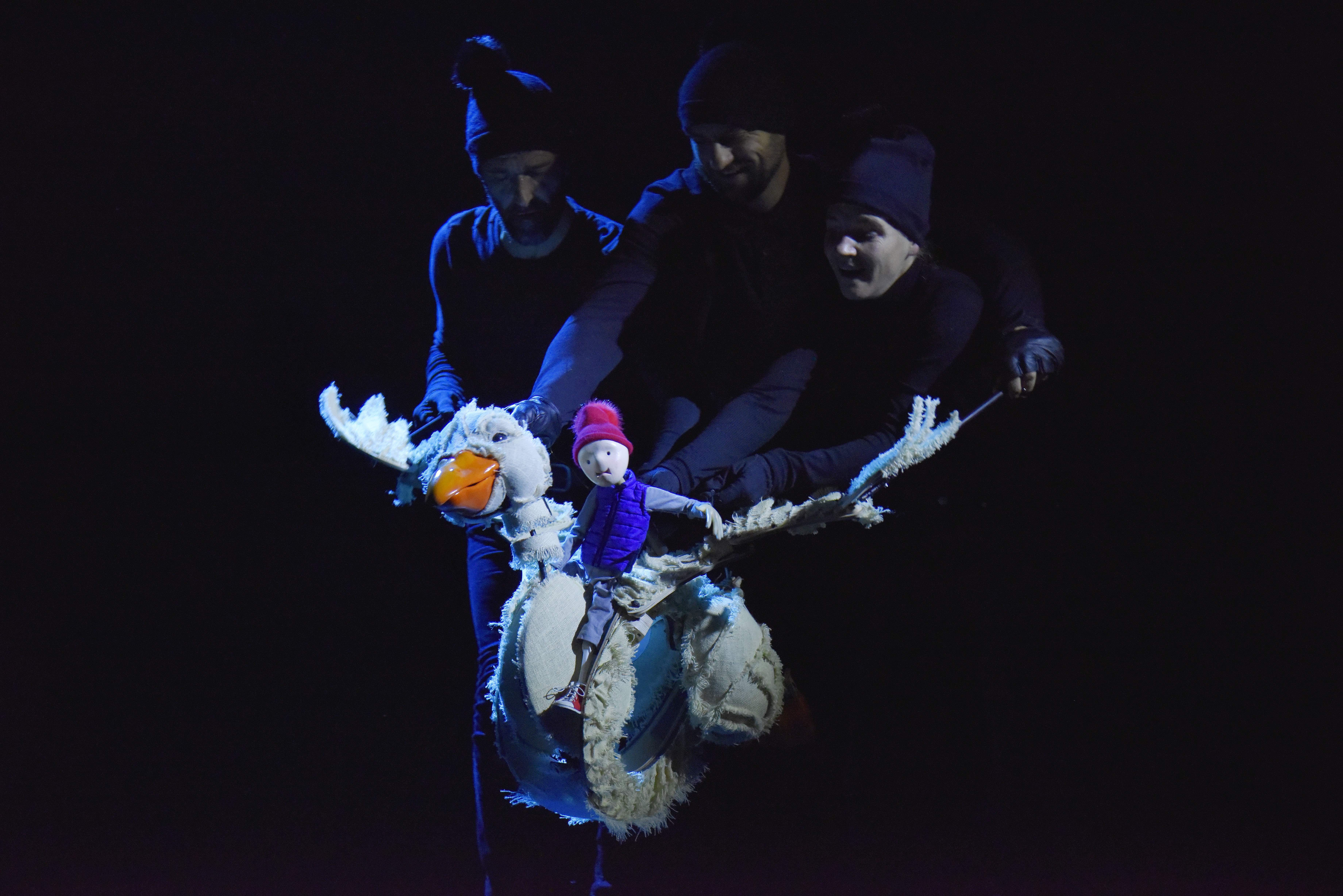 Trois comédiens marionnettistes font "voler" une oie blanche sur le dos de laquelle est assis Nils, personnage principal de cette histoire.